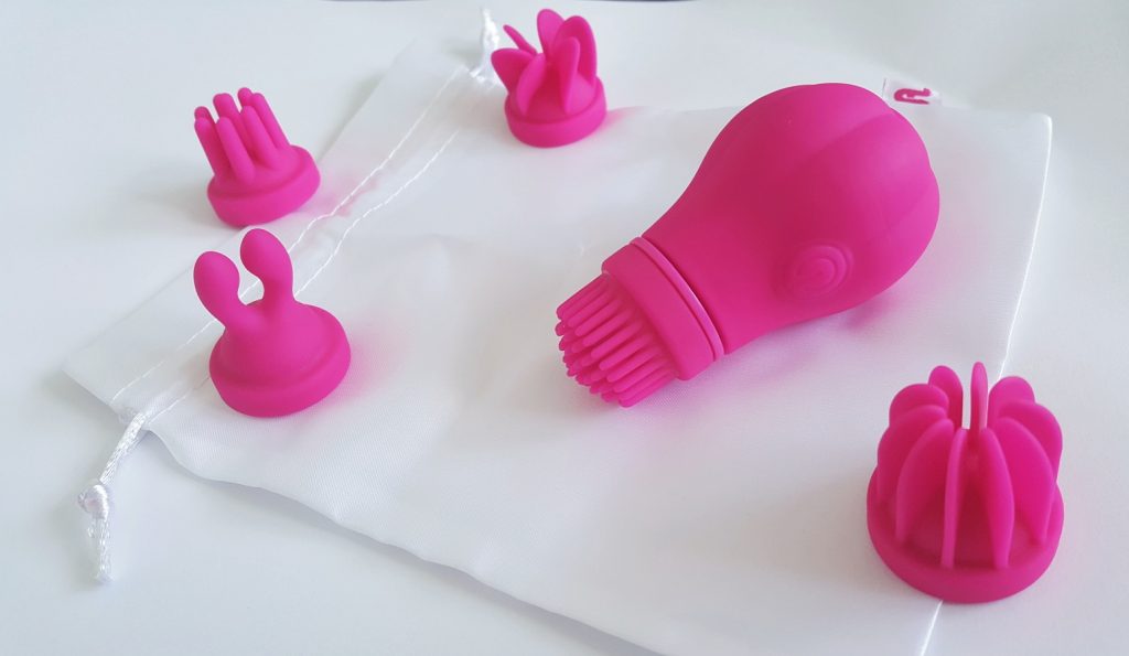 Photo of the Adrien Lastic Caress and its attachments on top of the white satin storage pouch.