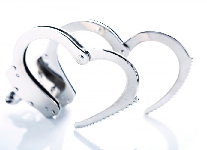 Photo of open metal handcuffs, each creating a heart shape