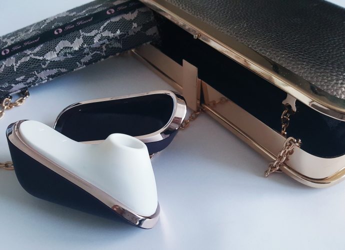 Feature photo for Satisfyer Pro Traveller Review. Satisfyer Traveller with a gold clutch bag and lace eyeshadow pallet.